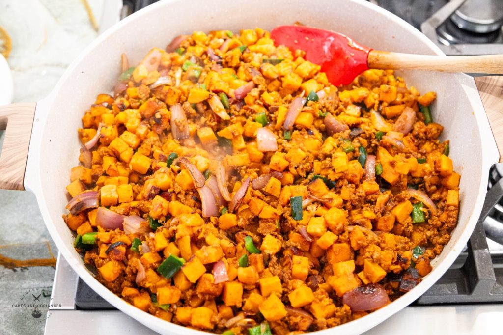 Sweet potatoes in a frying pan with cumin, poblano, red onion, soyrizo/chorizo, and coriander.