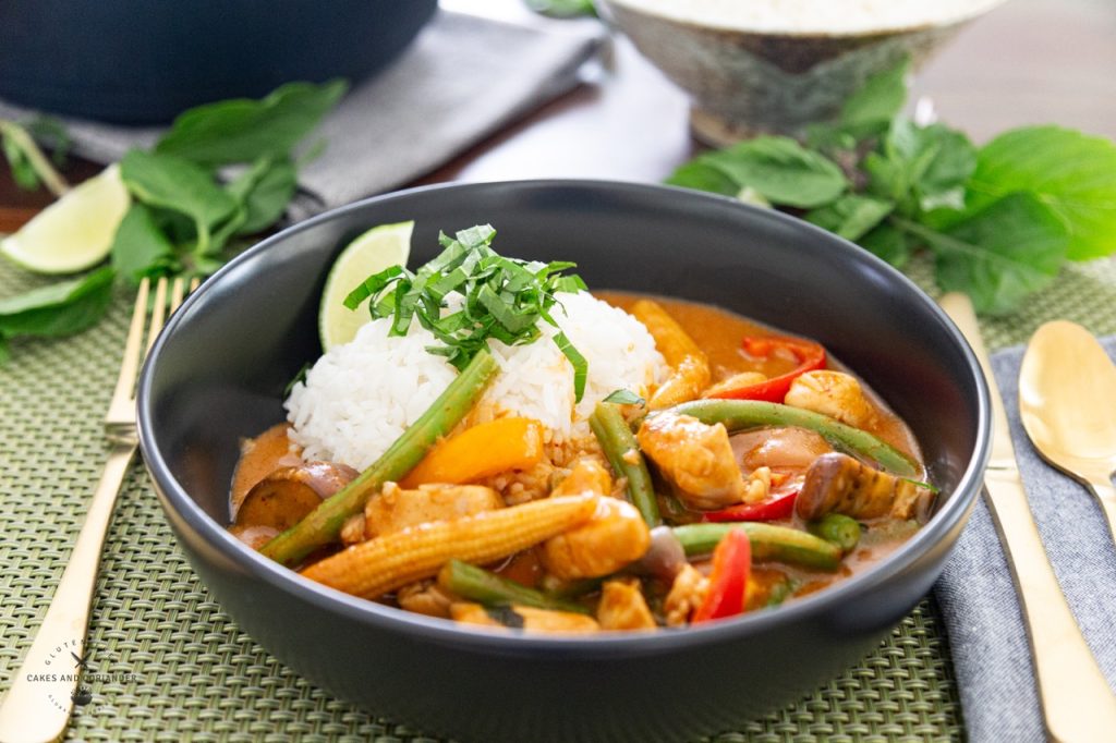 Sideview of Peanut Butter Curry recipe with Jasmine rice plated in a shall black bowl with green beans, eggplant, thai basil, chicken, and bell peppers